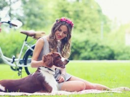 Eine junge Dame mit Blumenkranz macht mit ihrem Hund ein Picknick im Park; Fahrrad neben Picknick-Decke.
