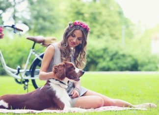 Eine junge Dame mit Blumenkranz macht mit ihrem Hund ein Picknick im Park; Fahrrad neben Picknick-Decke.
